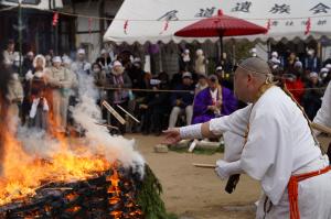 燃える護摩壇に護摩木を投げ入れる行者の写真